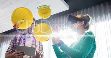 Digital composite image of emojis flying by couple using VR glasses and tablet computer at home