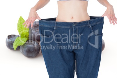 Midsection of woman in loose jeans by blueberries representing weight loss concept