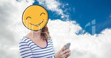 Woman with emoji over face using smart phone against sky