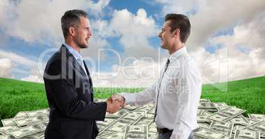 Side view of businessmen shaking hands with money in background