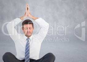 Business man meditating with hands over head against grey wall
