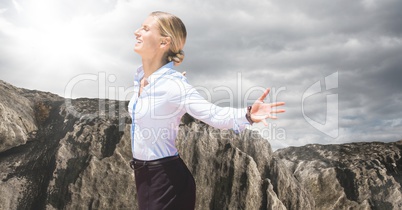 Business woman enjoying sun against rock and cloudy sky