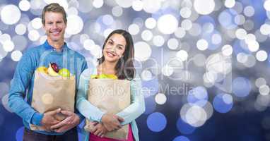 Happy couple carrying fruits in paper bag over bokeh