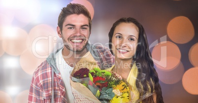 Portrait of happy man by woman holding flowers over bokeh