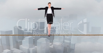 Businesswoman with arms outstretched standing on rope over city