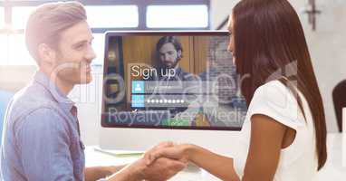 Man and woman shaking hands with sign up page on monitor in background