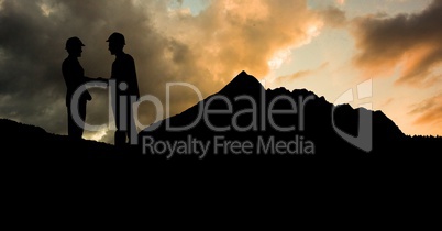 Silhouette male architects shaking hands on mountain against cloudy sky during sunset