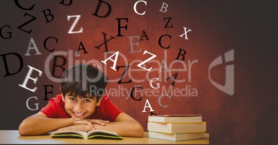 Happy boy with book leaning on table against flying letters