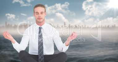 Business man meditating against water and blurry skyline with flare