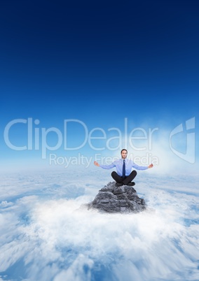 Business man meditating on mountain peak in the clouds