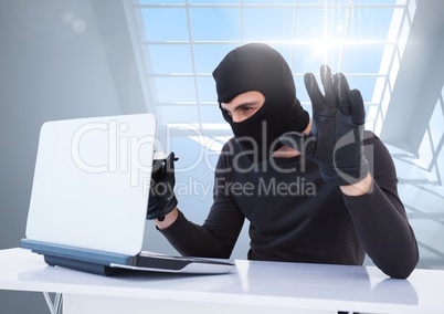 Criminal in hood with laptop in front of window