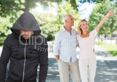 Criminal in hood in front of couple walking in park