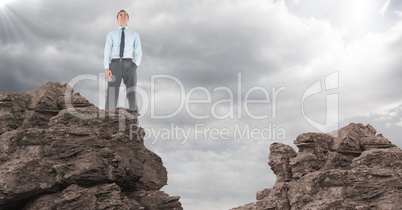 Business man hand in pocket on rocks against clouds with flare