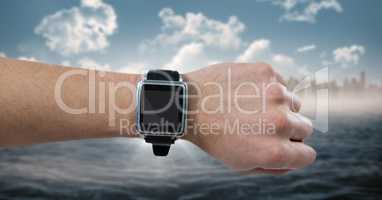 Hand with watch and flare against blurry skyline and water