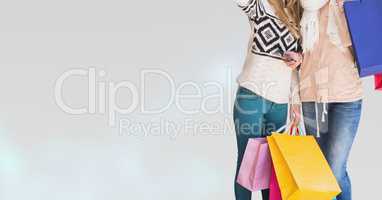 Midsection of female friends with shopping bags standing against white background