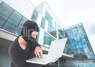 Criminal Man in balaclava on laptop in front of glass building