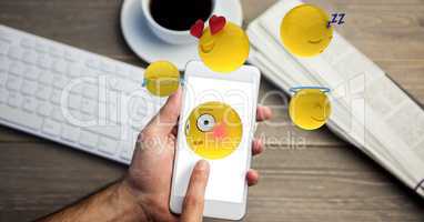 Digital composite image of emojis flying over hands using smart phone at table