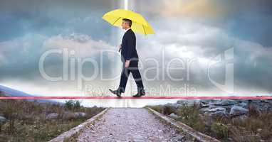 Businessman carrying umbrella while walking on rope