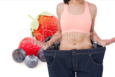 Midsection of woman in loose jeans by fruits representing weight loss concept