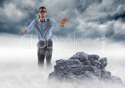 Business man blindfolded on misty mountain peak against storm clouds