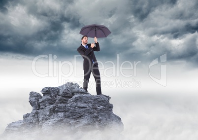 Business man standing on mountain peak with umbrella against stormy clouds