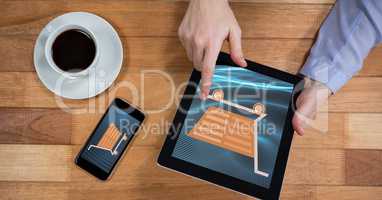 Hand touching shopping cart icon on tablet PC by mobile phone and coffee cup
