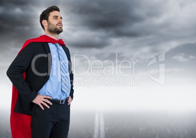 Business man superhero with hands on hips against road and grey sky with flare