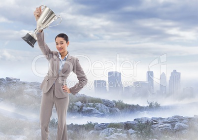 Business woman with trophy on misty mountain peak against skyline