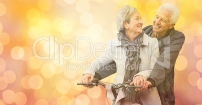 Happy senior couple riding bicycle over bokeh