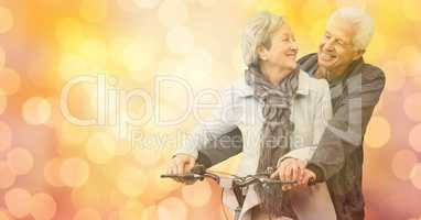 Happy senior couple riding bicycle over bokeh