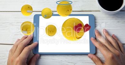 Digitally generated image of emojis flying over hand using tablet computer by drink on table