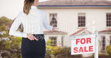 Rear view of businesswoman with fingers crossed standing by for sale sign