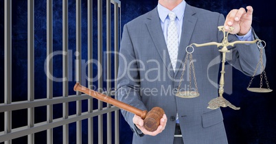 Businessman holding judge gavel and scales by prison cell