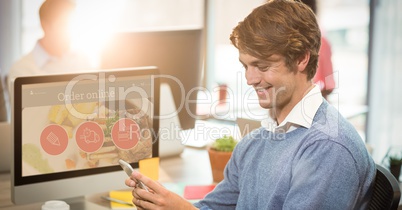 Smiling businessman using mobile phone at computer desk
