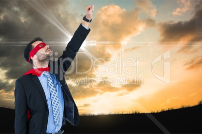 Businessman in super hero costume with hand raised against sky