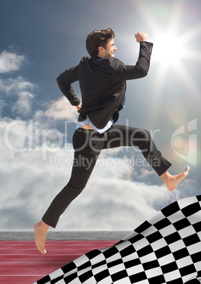 Business man jumping on track behind checkered flag and against sky with sun