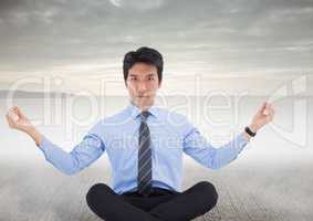 Business man meditating on concrete ground against grey sky