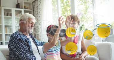 Digital composite image of emojis flying by family while girl using VR glasses while sitting on sofa