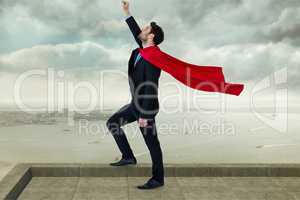 Businessman wearing cape with arm raised  while standing against cloudy sky