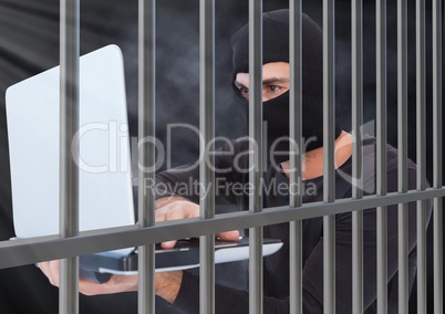 Criminal in balaclava with laptop behind prison bars