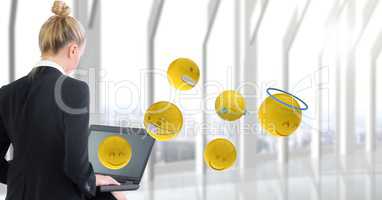 Rear view of businesswoman using laptop while emojis flying in office