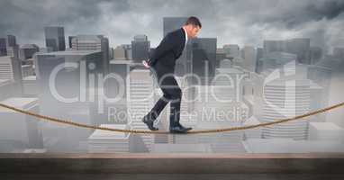 Digital composite image of businessman walking on rope against cityscape