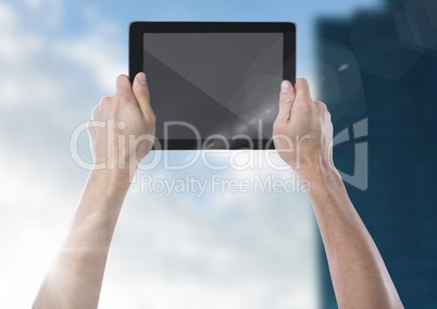 Hand with tablet against blurry building with flare