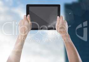 Hand with tablet against blurry building with flare