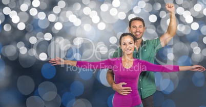 Smiling man and woman with arms raised over bokeh
