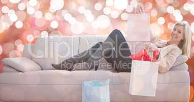 Happy woman with shopping bags lying on sofa over bokeh