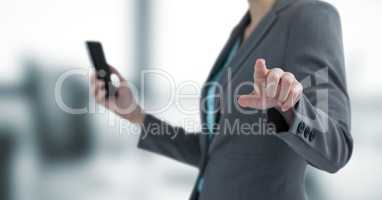 Midsection of businesswoman holding mobile phone while touching transparent screen
