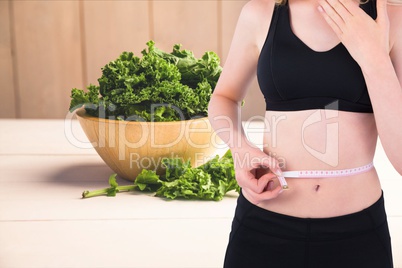 Midsection of woman measuring waist with kale in background