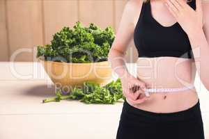 Midsection of woman measuring waist with kale in background