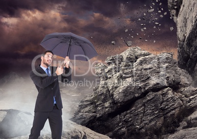 Business man standing with umbrella and mist against falling rocks